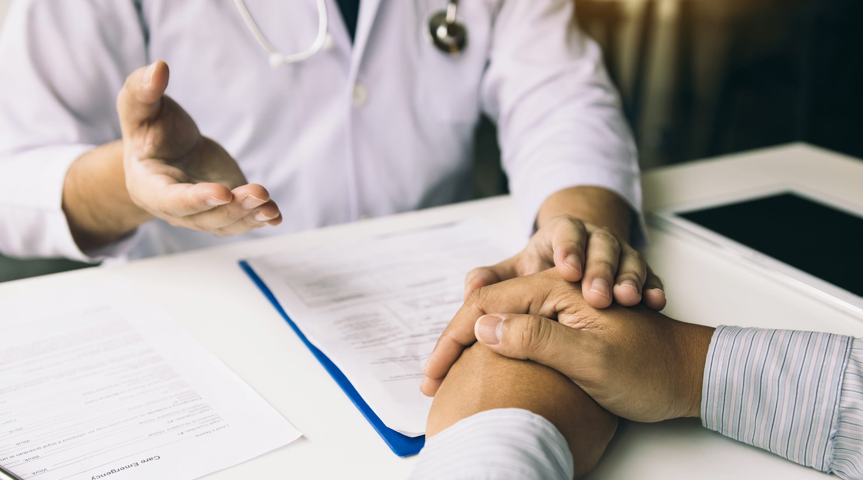 A doctor holds their hand over a patient's while explaining a situation.