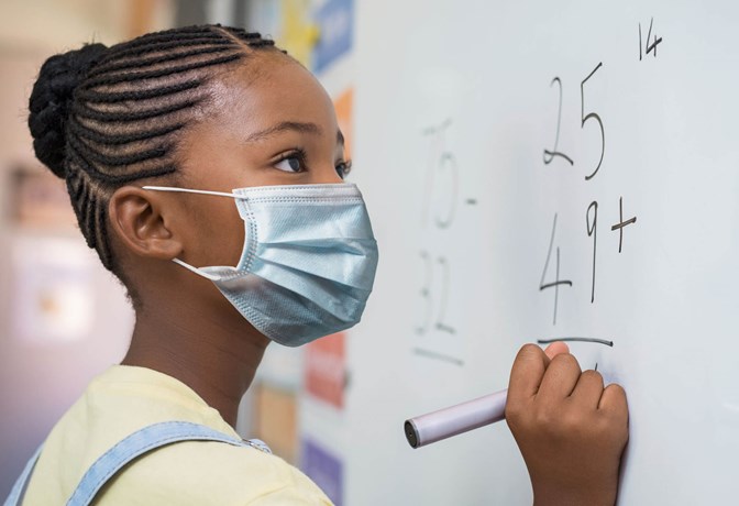 Girl wearing a mask writing on white board
