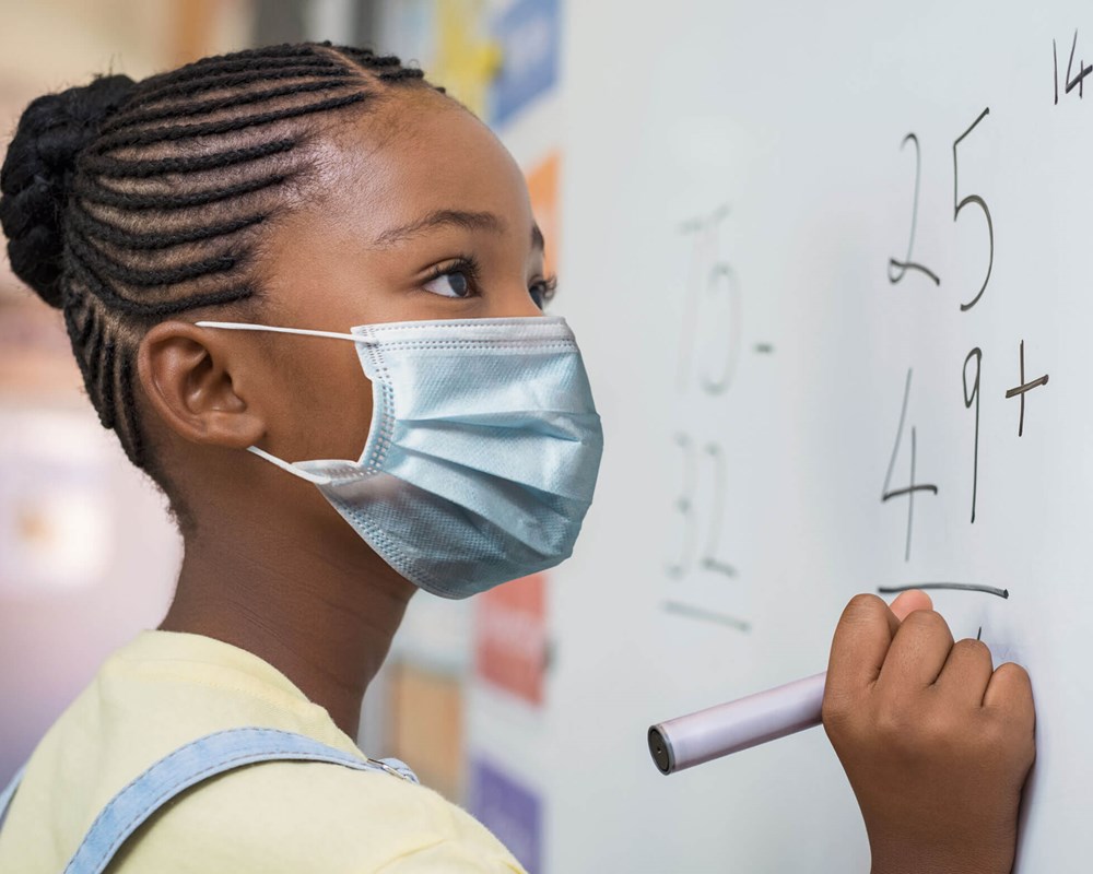 Girl wearing a mask writing on white board