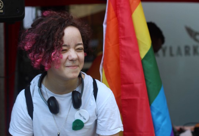 Young person in front of rainbow flag