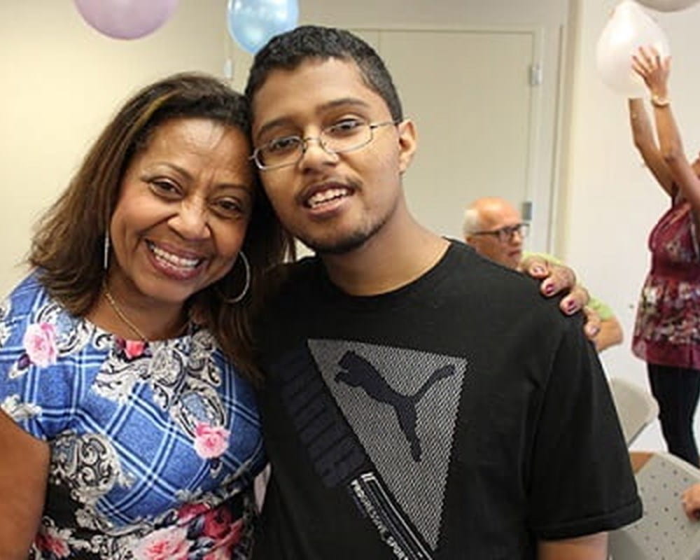 A man of colour and a woman of colour standing next to each other and smiling with balloons in the background.