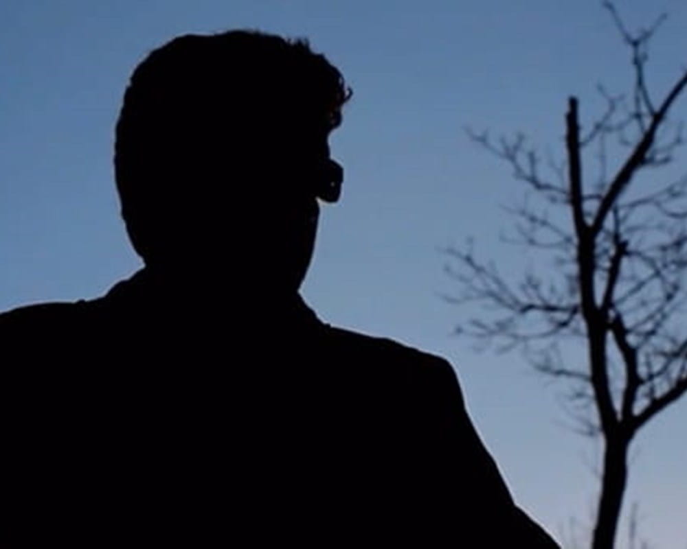 A black shadow of a person with glasses on a gradient blue background with a tree on the right.