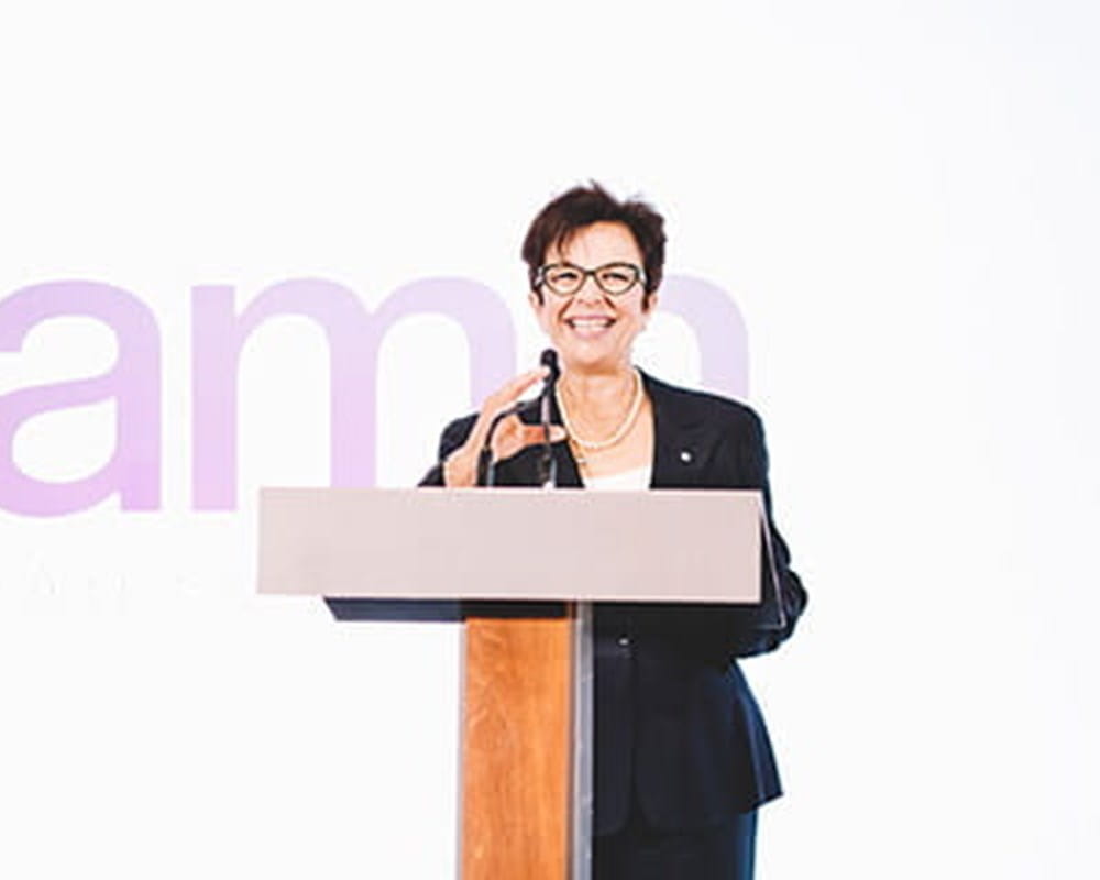 CEO, Catherina Zahn in a black blazer talking in front of a wooden podium.