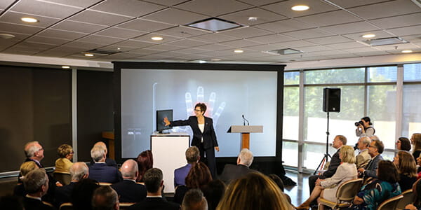 CEO, Catherine Zahn standing in front of an audience scanning her hand against a screen and it projecting it onto a screen. 