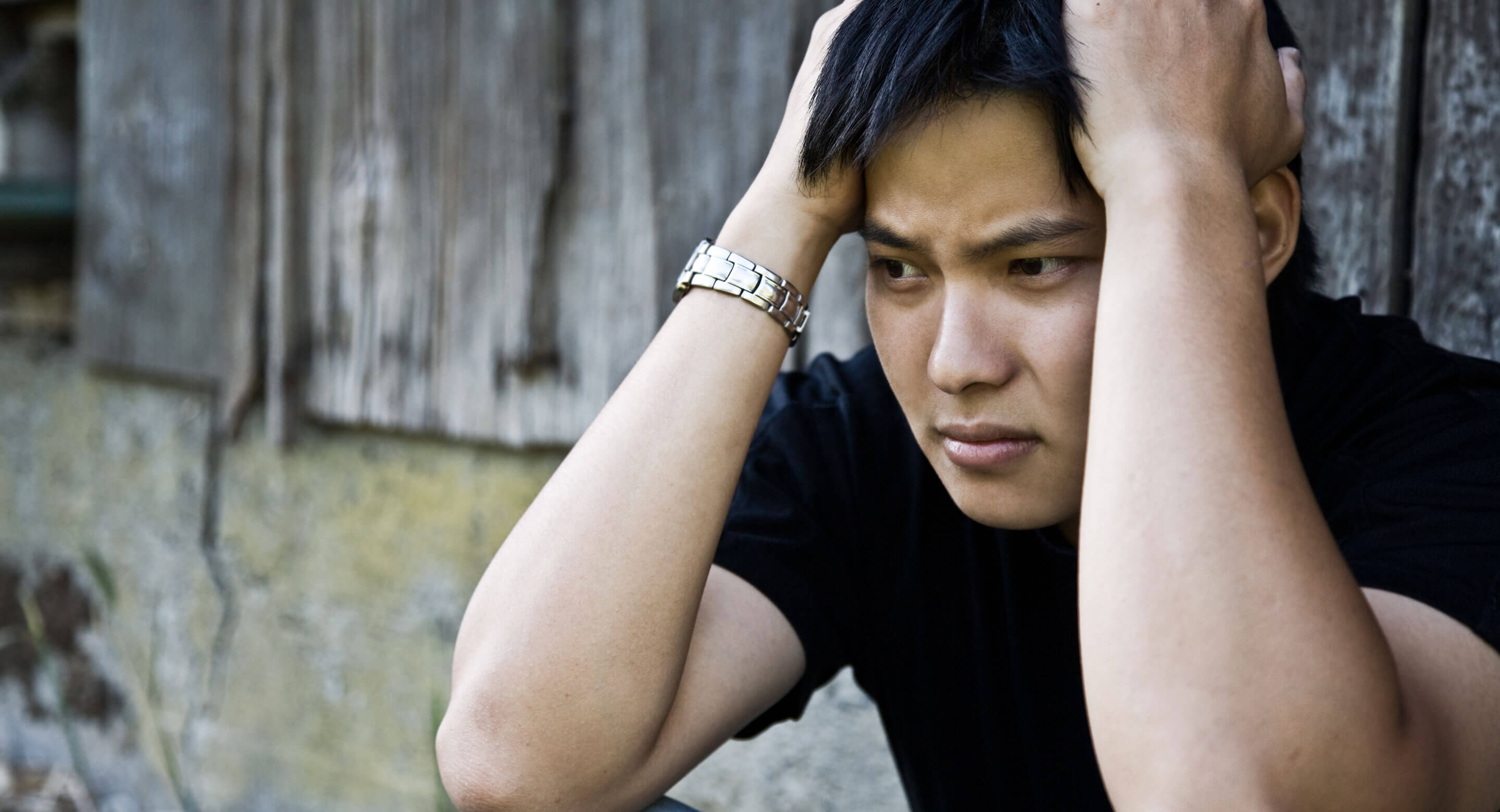 Young Asian man holding his head, looking sad.