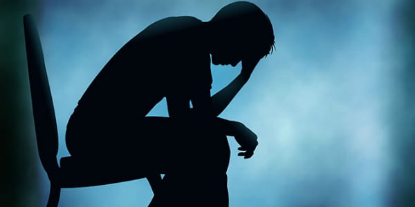 A shadow of a person sitting on a bench looking upset with a blue background. 