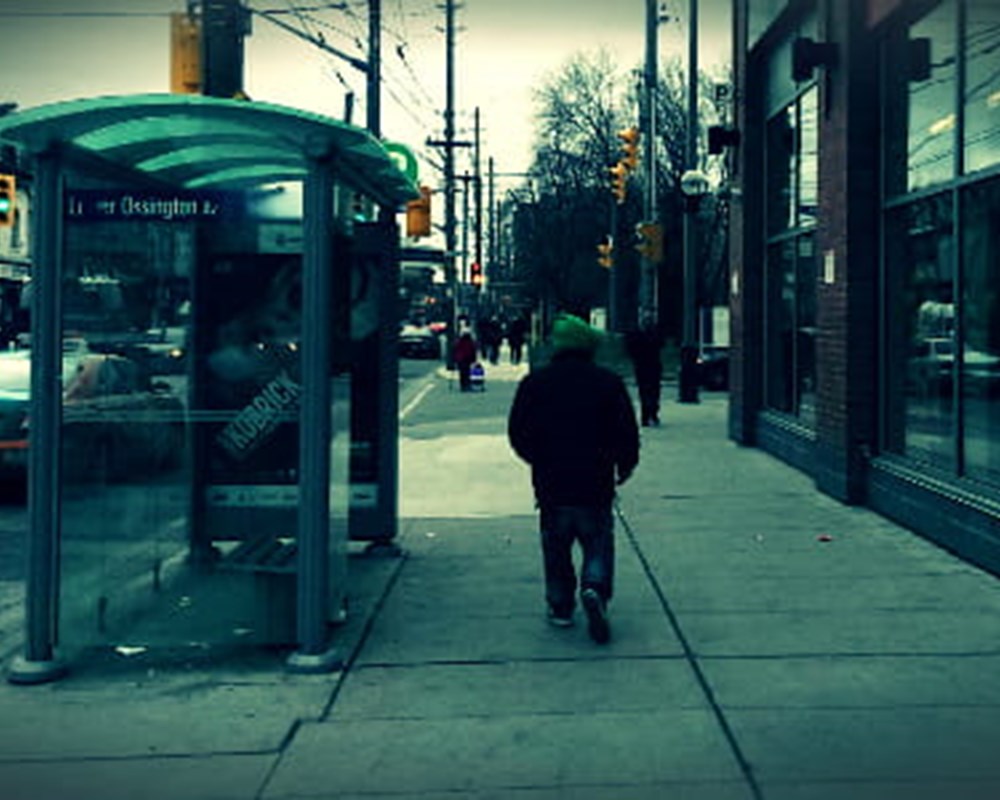 A blue tinted image of a person walking down Ossington Street.