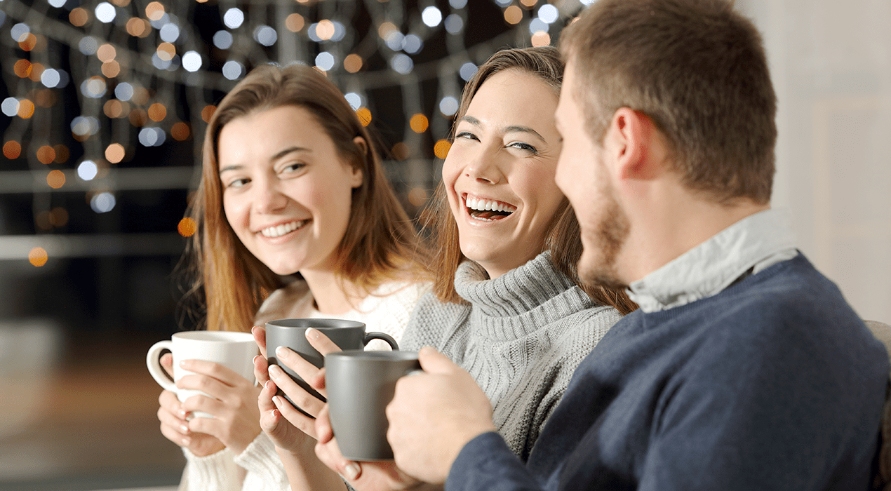 Three adults enjoying hot beverages in mugs against a festive background.