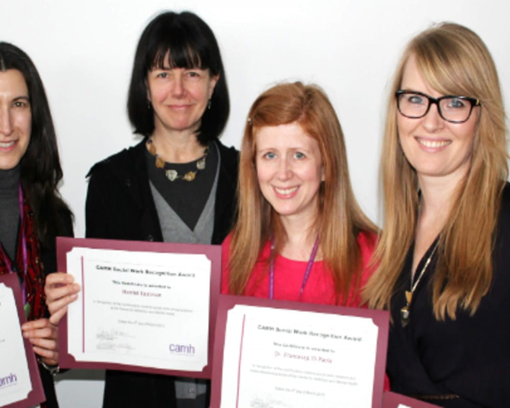 Four women smiling and holding a Social Work Recognition Award in front of their chest.