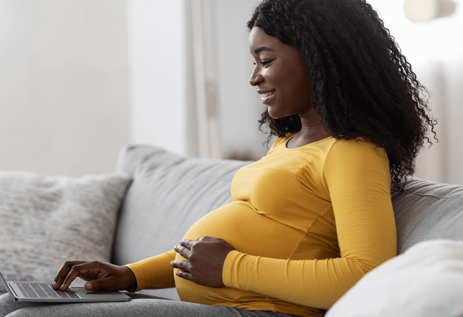 Black pregnant woman using laptop at home.