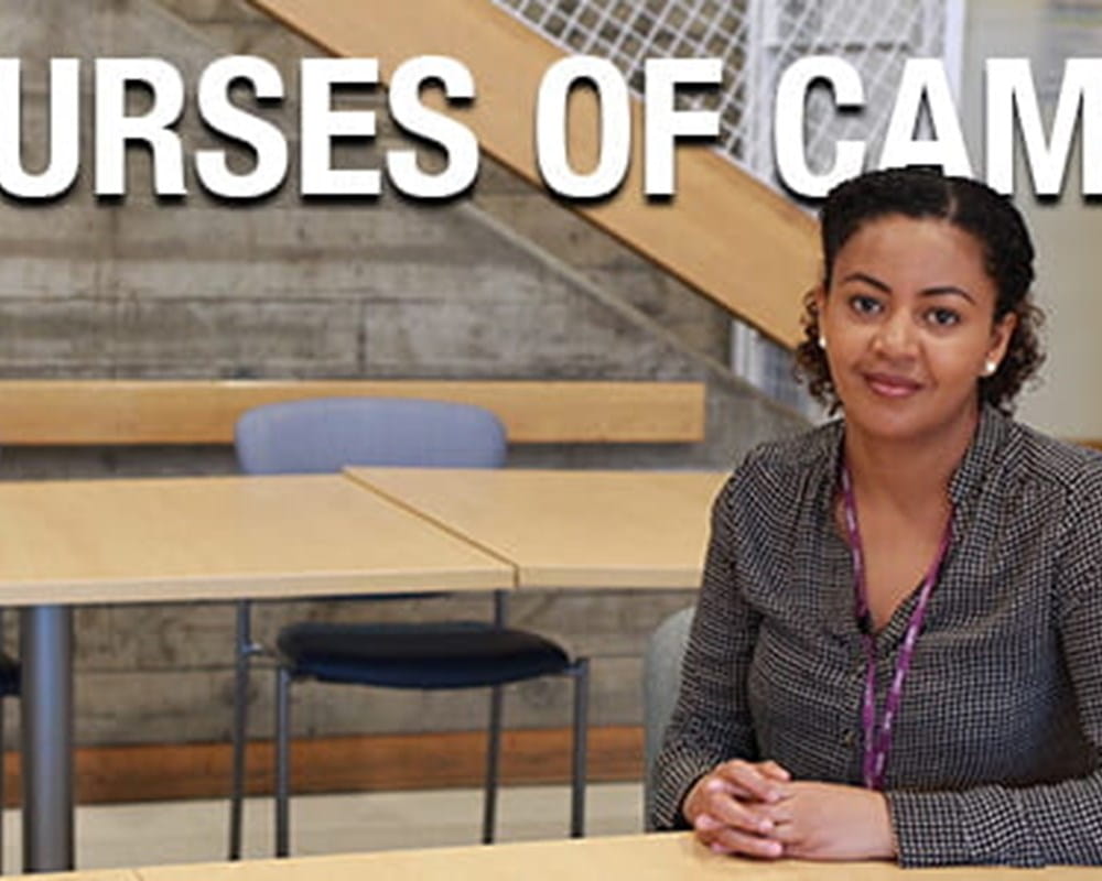 A woman of colour who is a nurse at CAMH wearing wearing a checkered blouse with a CAMH lanyard, sitting at a table smiling, with the phrase