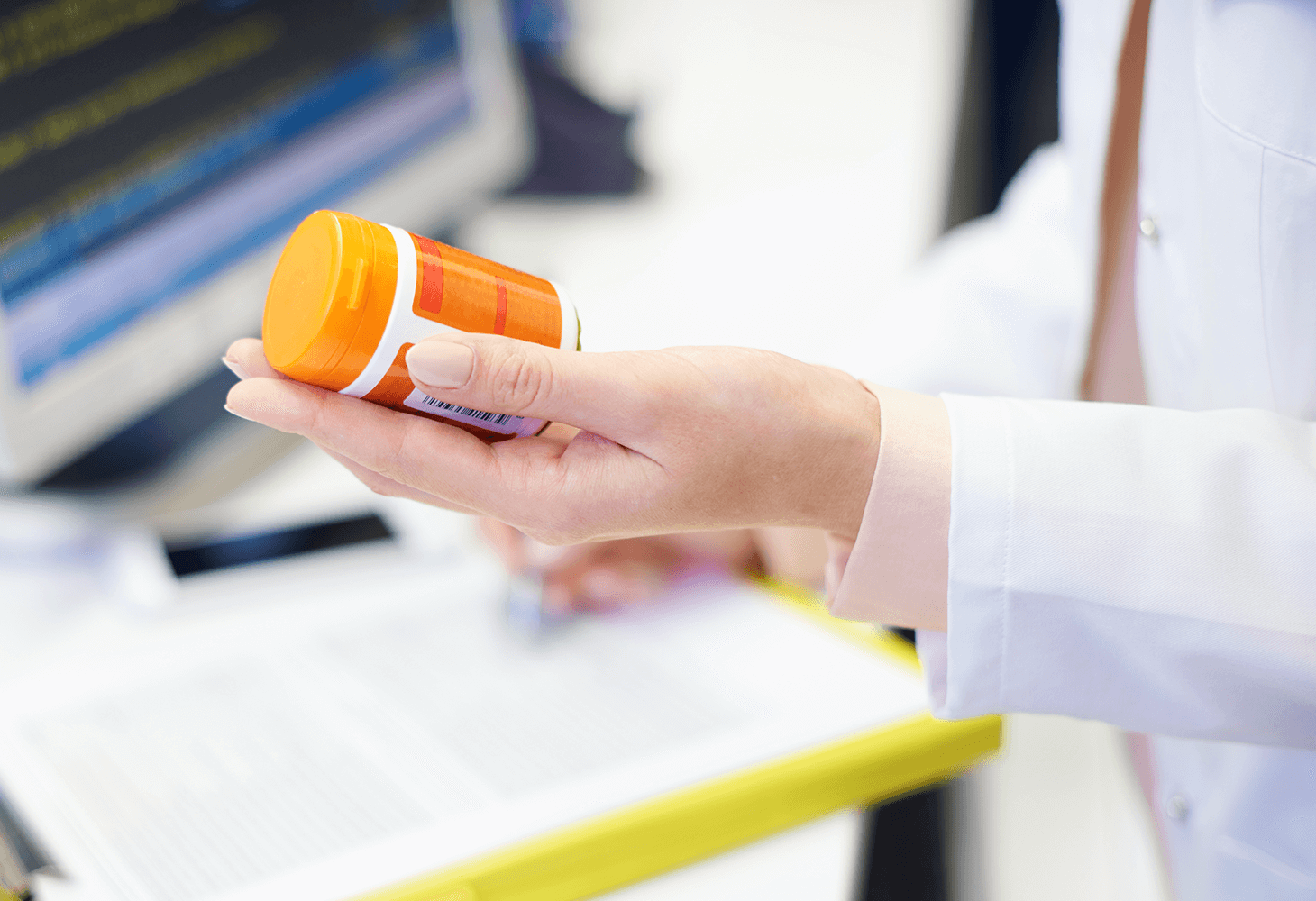 A physician holds a bottle of pills while making notes on patient's file